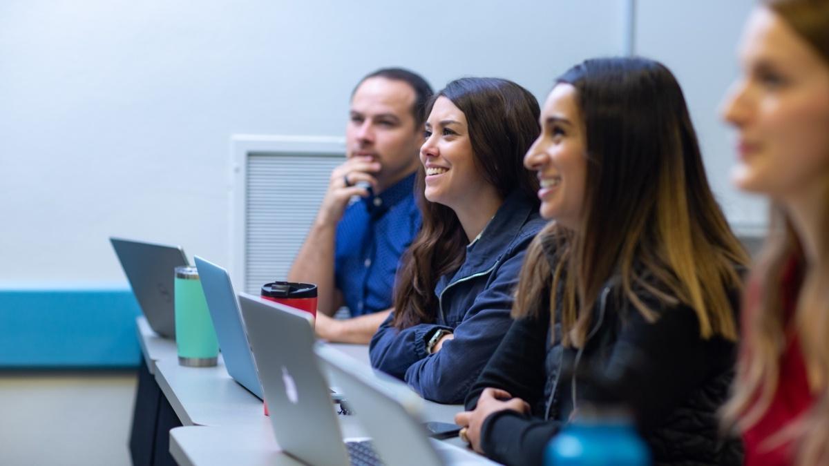 for students sit at a row of desks listening to a lecture